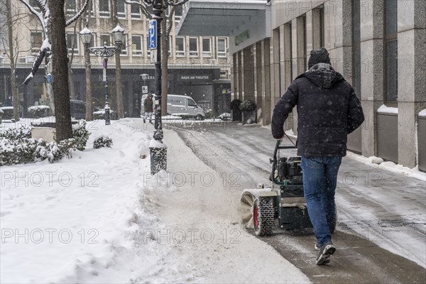 Private winter service, snow sweeper in front of a commercial building in the city centre of Essen,