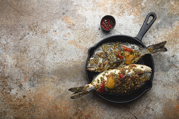 Two raw fishes dorado stuffed with vegetables and seasonings ready to be cooked laying in black