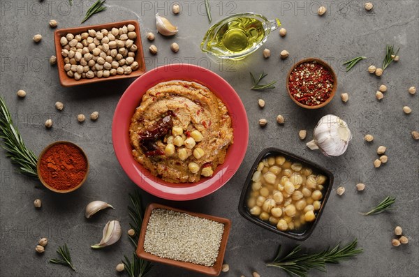 Hummus topped with chickpeas, olive oil and sun dried tomato on stone table with different spices