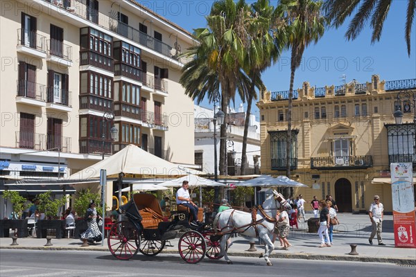 Horse-drawn carriage with passengers on a sunny street, surrounded by old buildings, Sanlúcar de