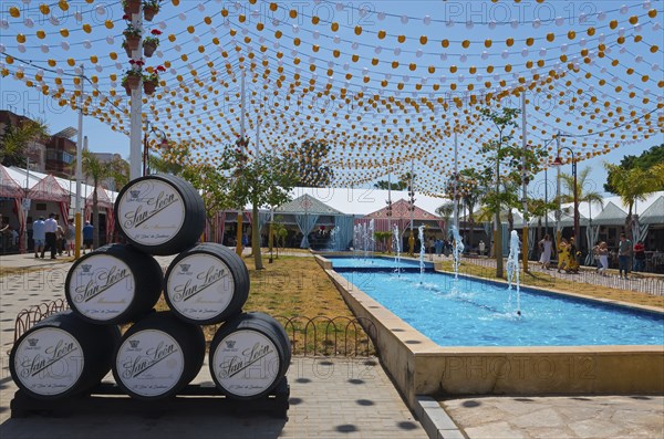 Colourful fairy lights over barrels next to a water basin, festive atmosphere, Feria de la