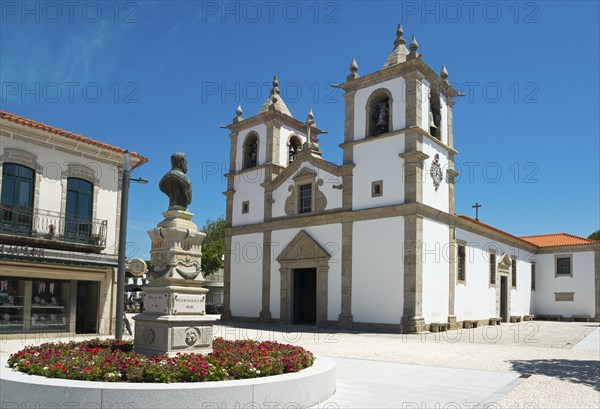 A church with a double tower stands on a sunny square with a flower bed, Igreja Matriz de