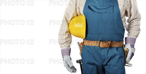 Middle aged contractor in overalls with tool belt holds yellow hard hat in his hands on white