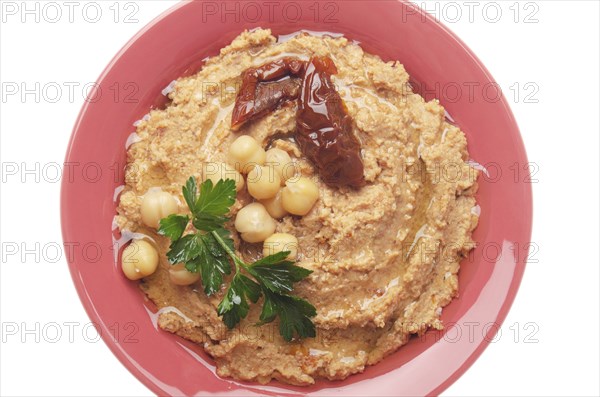 Flat lay view at hummus topped with beans, sun dried tomatoes and green coriander leaves isolated