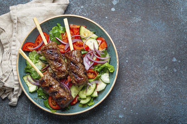 Grilled skewer meat beef kebabs on sticks served with fresh vegetables salad on plate on rustic