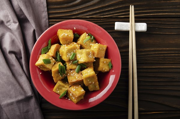 Flat lay view at crispy deep stir fried tofu cubes with chives in clay dish on wooden kitchen table