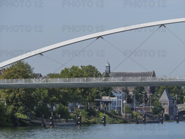 View of a modern bridge and historic buildings along a river in summer, maastricht. netherlands
