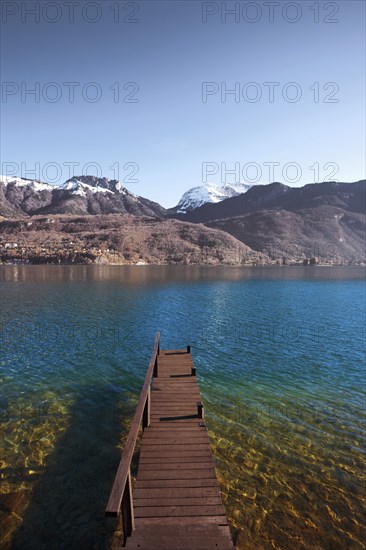 An old wooden pier faces the snow-capped mountains of the French alps on beautiful Lake Annecy.