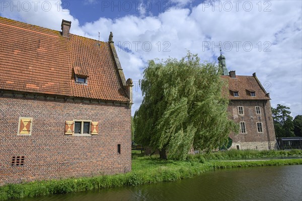 Historic castle with red tiled roofs and a moat, surrounded by trees and clouds, Raesfeld, North