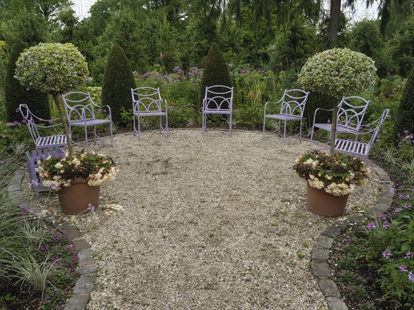 Round garden area with purple chairs and two potted plants, surrounded by green vegetation and