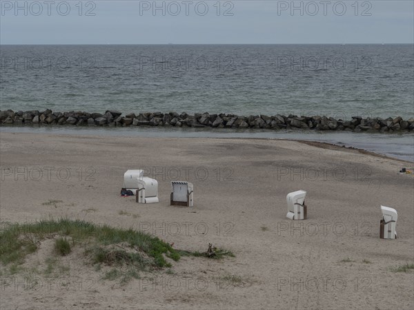 An empty beach with a few beach chairs, a calm sea and stone breakwaters in the background. A quiet