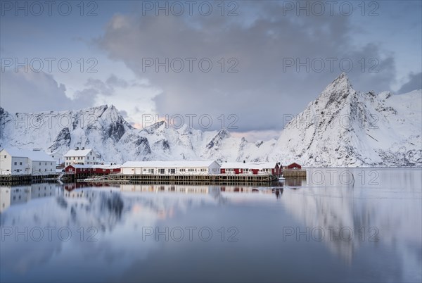 Rorbuer huts of Hamnoy at the fjord, snowy mountains in the background, Hamnøy, Reine, Moskenesøya,