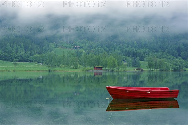A small, red boat on a calm lake, idyll, surrounded by fog and green nature, Stryn, Mindesundet,