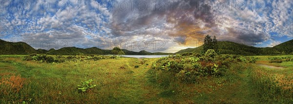 360° panorama with a meadow and mountains in the background, a lake in the distance, dramatic sky