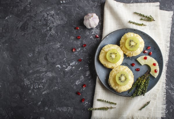 Pieces of baked pork with pineapple, cheese and kiwi on black background, top view, copy space