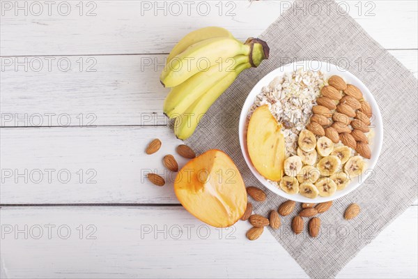 A plate with muesli, almonds, banana, sliced persimmon on a white wooden background. top view. copy