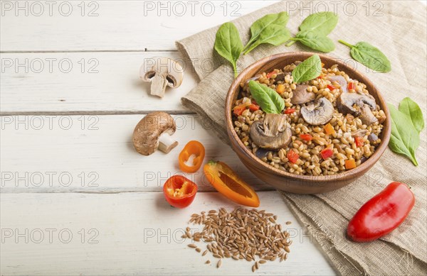 Spelt (dinkel wheat) porridge with vegetables and mushrooms in wooden bowl on a white wooden