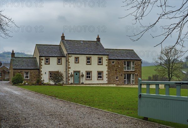 View of an older rendered house with a stone outbuilding behind a lawn and in front of a gravelled
