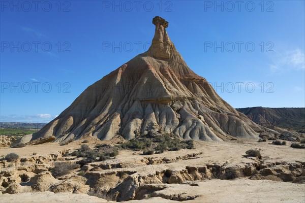 A large rock rises out of a sandy desert under a clear blue sky, Castildetierra, Bardenas Reales
