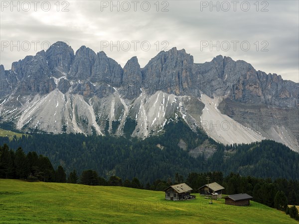 Alpine huts in front of the Geisler peaks under a cloudy sky, Villnöss Valley, Sass Rigais,