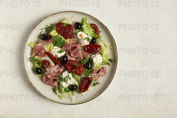 Salad with dried tomatoes, prosciutto, soft cheese, olives, homemade, top view