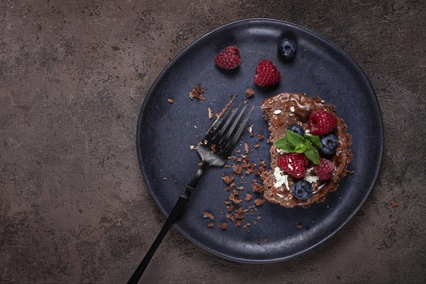 Half-eaten chocolate tartlet, on a plate, stuffed with cottage cheese and berries, breakfast,