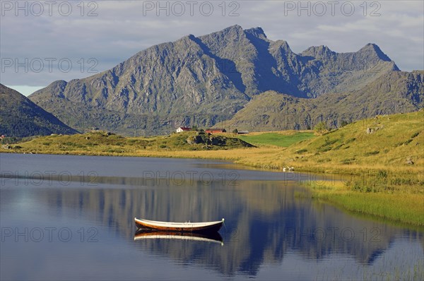A small wooden boat floats on a calm lake with majestic mountains in the background, Leknes,