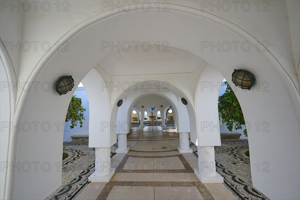 Curved arches in an inner courtyard with white walls, ornate lamps and lots of plants, thermal