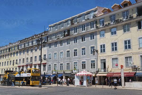 Lively street with many shops and tall buildings, people and a bus under a sunny sky, house with
