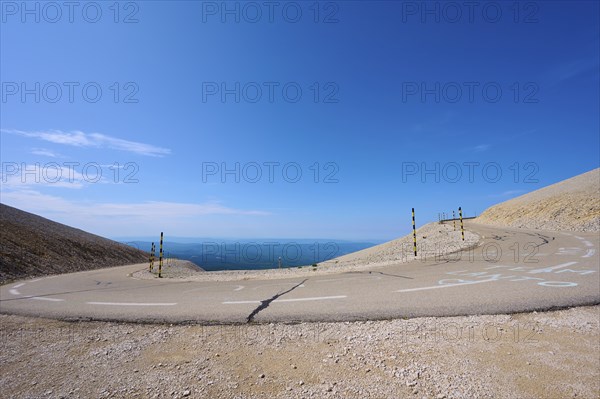 An empty mountain road with a hairpin bend under a clear blue sky and barren landscape, Mont