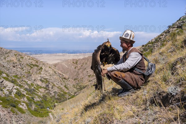 Traditional Kyrgyz eagle hunter with eagle in the mountains, near Kysyl-Suu, Kyrgyzstan, Asia