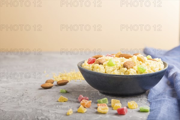 Millet porridge with candied fruits and almonds in blue ceramic bowl on a gray and orange