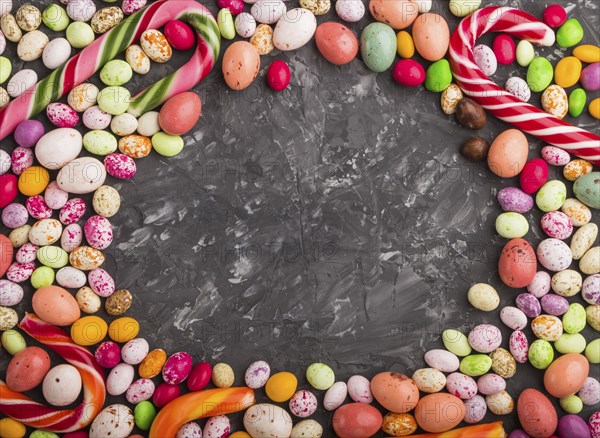 Colorful frame of multicolored candies on a black concrete background. Christmas cane, chocolate