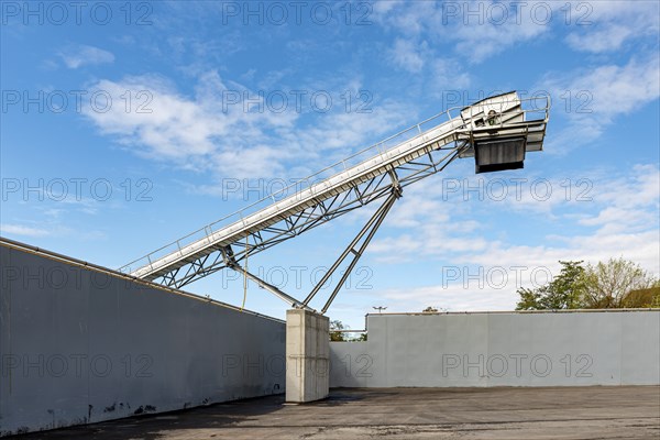 Large conveyor belt towers over a wall, contrasting with blue sky