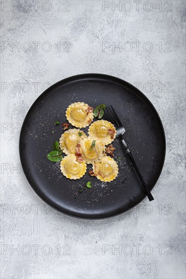 Fresh ravioli, with butter, spices and herbs, fried bacon, on a black plate, top view, dark