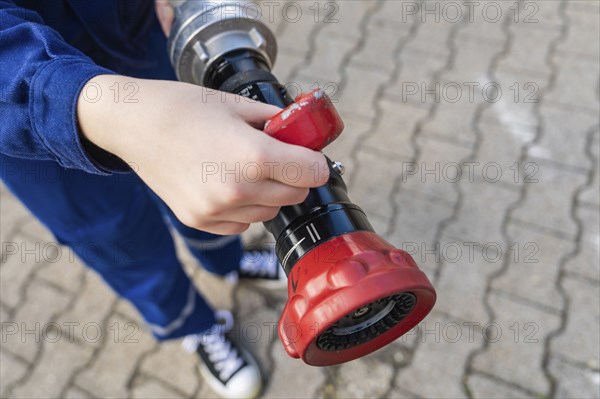 Child holding a fire hose with red handles on a cobbled floor, fire brigade, Enzklösterle, Black