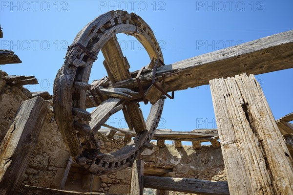 Close-up of a wooden cogwheel and wooden beams in an abandoned old mill under a clear sky,