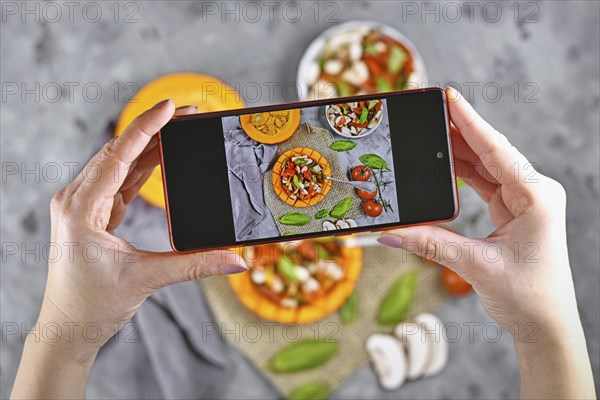 Taking photo of food with hands holding mobile phone with picture of vegan baked Red kuri squash