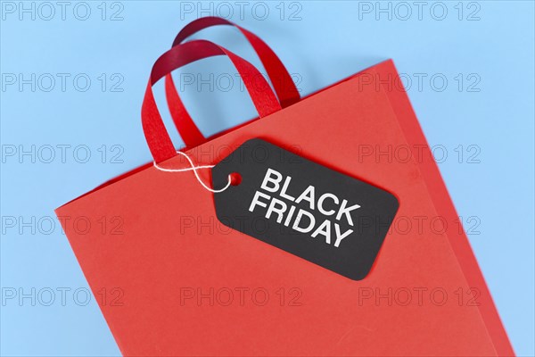 Black Friday sale label on red paper shopping bag on blue background