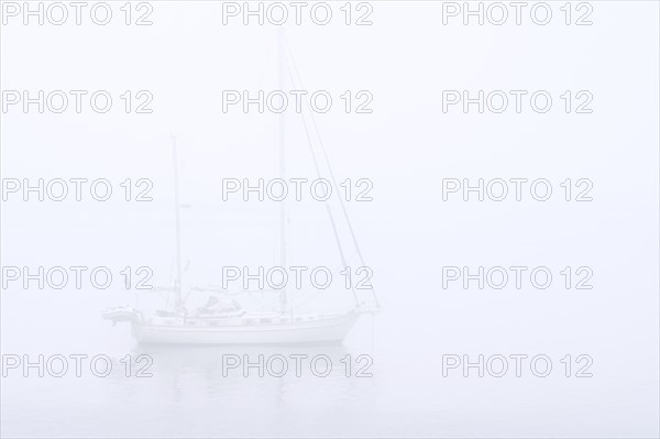 Sailboat, sailing boat, yacht with lowered sails anchored at sea during bad visibility due to thick