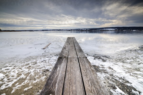 Frozen lake with wooden dock leading to the horizon, under a grey sky, campsite, Hegne, Lake