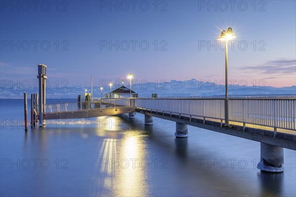 An illuminated jetty over a calm lake with mountains in the background in blue twilight, harbour,