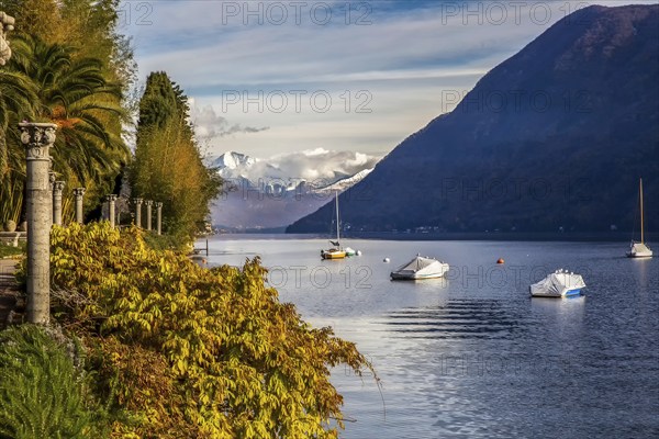 Sheltered sailboats in lake lugano, view from park Helenium with columns and snow-capped mountains