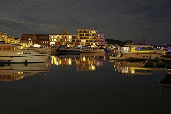 Marina at night with illuminated buildings and reflection in the water, Waren, Müritz,