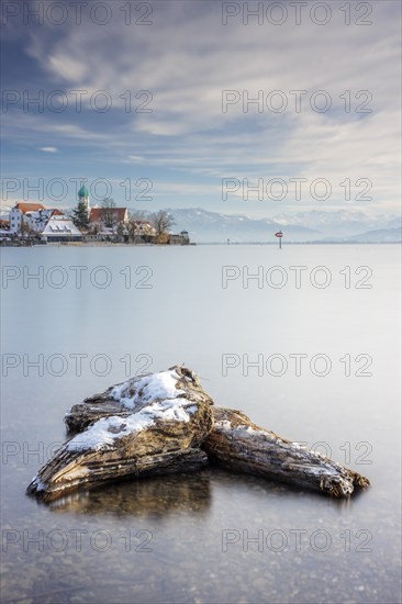 Wooden trunks picturesque church of St. George on the lakeshore in front of snow-covered Pfänder on