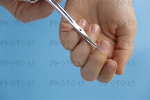 Stylish nude beige female nails using scissors on blue background. Modern trendy stylish Beautiful