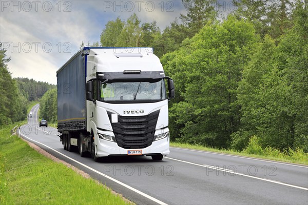White Iveco S-Way truck pulls curtainside semi trailer uphill along highway 52 on a day of summer.