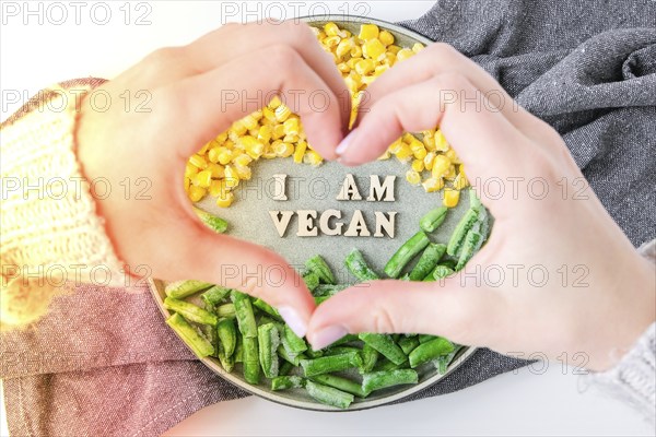 Female hands in shape of heart love I AM VEGAN text in plate. Veganism, vegetarian healthy