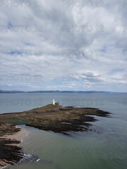 A view of the Mumbles Lighthouse in Swansea Bay at low tide with algae and rocks in the foreground