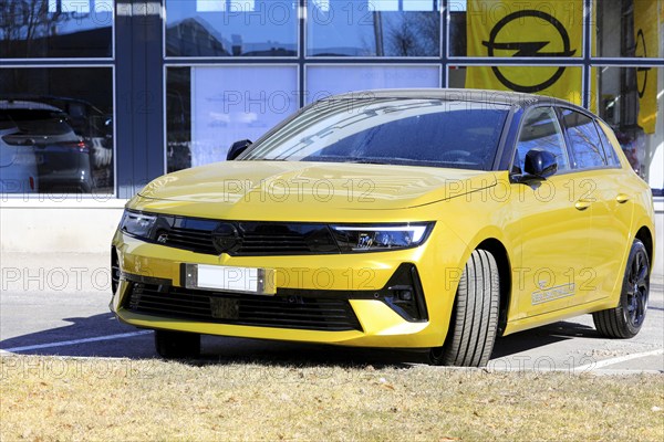 New, yellow Opel Astra parked outside a dealership. The new 6th generation of Astra is available